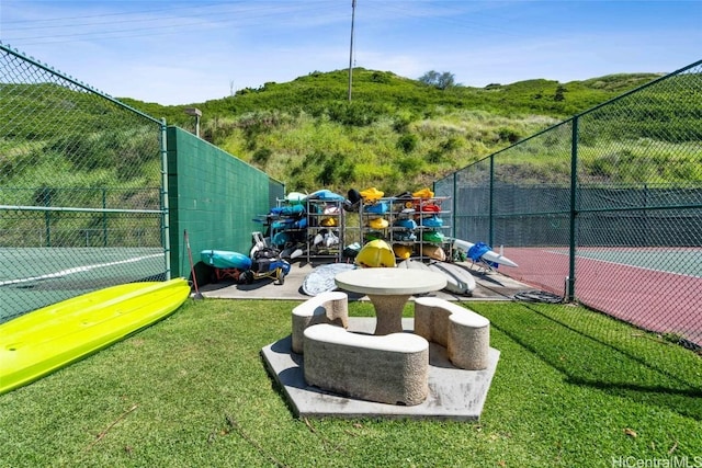 view of home's community with a tennis court, a yard, and fence