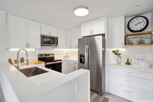 kitchen featuring stainless steel appliances, a peninsula, a sink, white cabinets, and light countertops