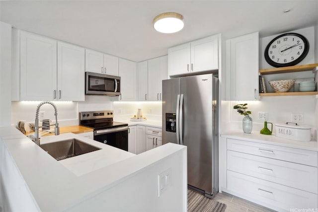 kitchen with a sink, light countertops, stainless steel appliances, white cabinetry, and a peninsula