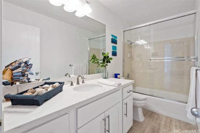 bathroom featuring wood finish floors, shower / bath combination with glass door, vanity, and toilet