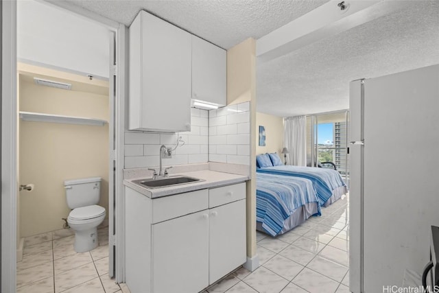 kitchen featuring white cabinets, freestanding refrigerator, a sink, light countertops, and backsplash