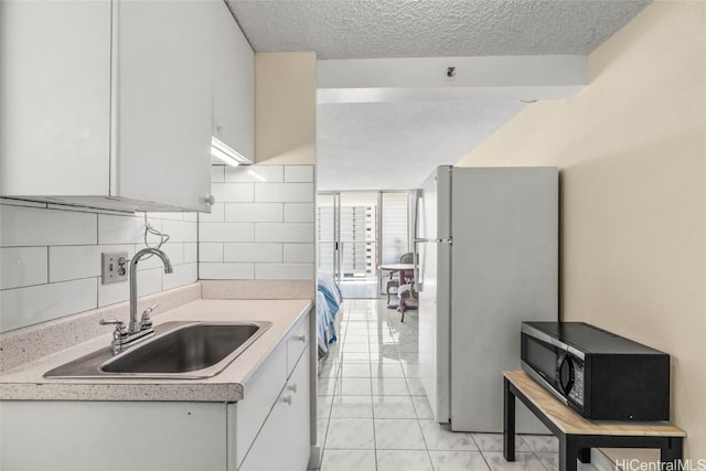 kitchen featuring black microwave, a textured ceiling, a sink, light countertops, and freestanding refrigerator