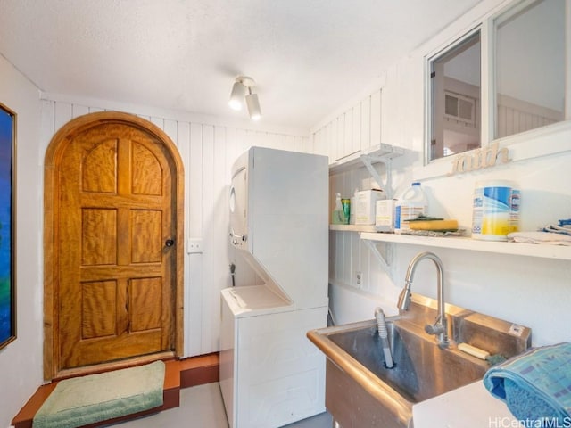 clothes washing area with stacked washer and dryer, a sink, and laundry area