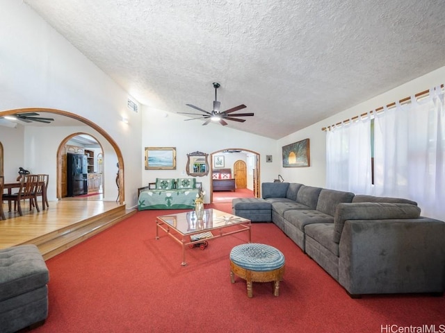 living area with arched walkways, ceiling fan, a textured ceiling, lofted ceiling, and carpet