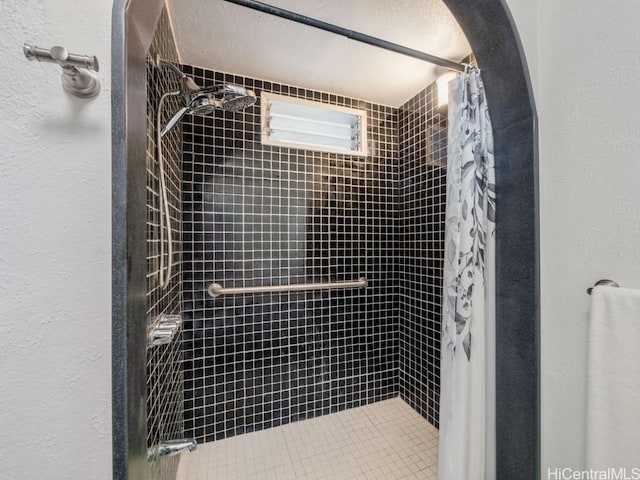 bathroom featuring a textured ceiling, a textured wall, and tiled shower