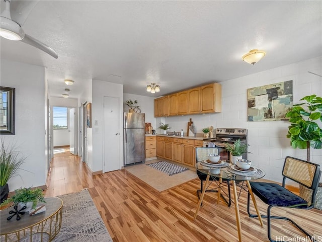 kitchen with concrete block wall, stainless steel appliances, light countertops, a sink, and light wood-type flooring