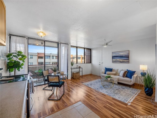 living room featuring a ceiling fan, light wood-style flooring, and a textured ceiling