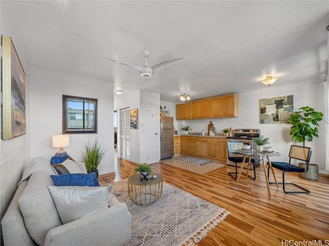 living room featuring concrete block wall, light wood-style flooring, and a ceiling fan