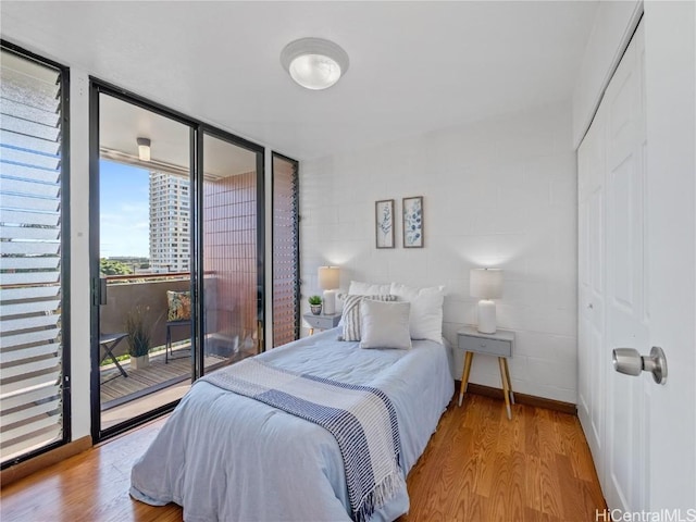 bedroom with baseboards, floor to ceiling windows, wood finished floors, and access to exterior