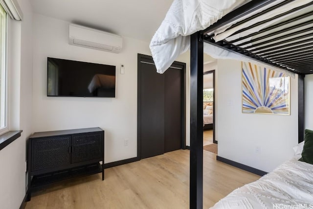 bedroom featuring light wood-type flooring, baseboards, and an AC wall unit