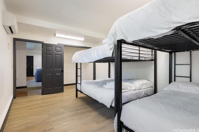 bedroom with an AC wall unit, light wood finished floors, and baseboards