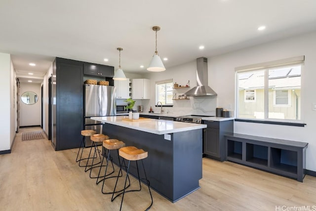 kitchen featuring a center island, open shelves, appliances with stainless steel finishes, wall chimney range hood, and a kitchen bar