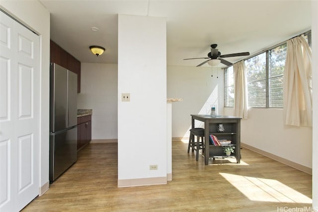 kitchen featuring baseboards, light wood finished floors, ceiling fan, and freestanding refrigerator