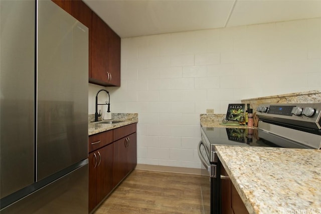 kitchen with light stone counters, wood finished floors, stainless steel appliances, and a sink