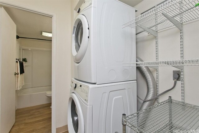 clothes washing area with laundry area, wood finished floors, and stacked washer and clothes dryer