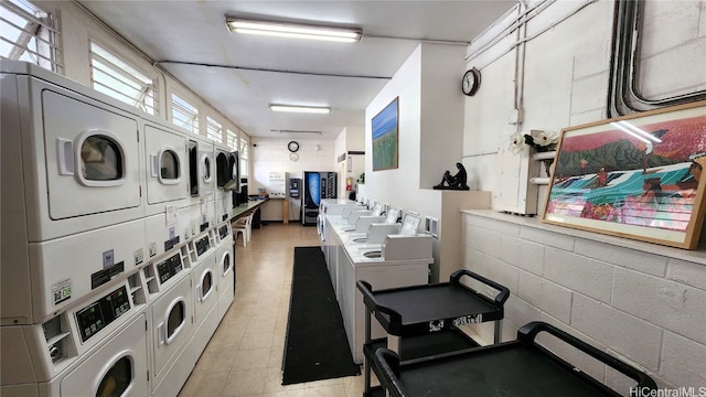 community laundry room with concrete block wall, stacked washing maching and dryer, light floors, and washing machine and clothes dryer