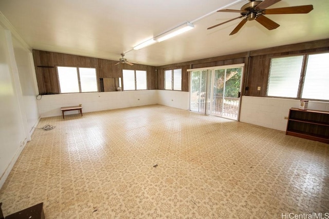 unfurnished room featuring lofted ceiling, wood walls, a wealth of natural light, and a ceiling fan