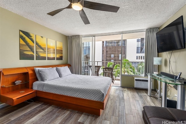 bedroom featuring a wall mounted AC, a ceiling fan, expansive windows, a textured ceiling, and wood finished floors