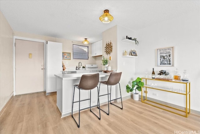 kitchen featuring a peninsula, range with electric stovetop, white cabinets, light wood-style floors, and light countertops