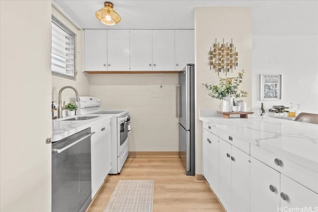 kitchen with light stone counters, stainless steel appliances, a sink, white cabinetry, and light wood-style floors