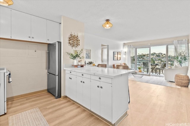 kitchen with open floor plan, freestanding refrigerator, a peninsula, light countertops, and light wood-type flooring