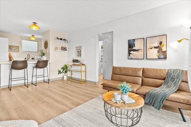 living area featuring light wood-type flooring, a textured ceiling, and baseboards