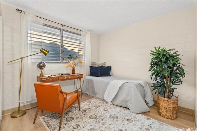 bedroom featuring concrete block wall, a textured ceiling, and wood finished floors