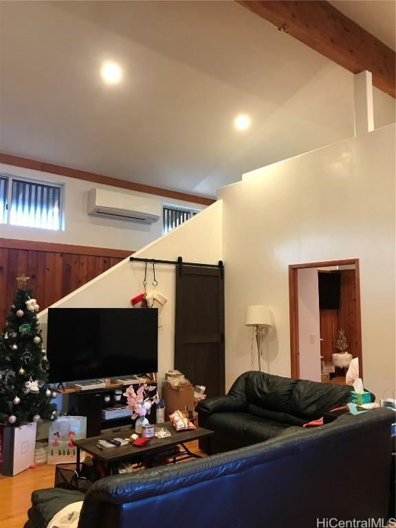 living area featuring a barn door, wood finished floors, high vaulted ceiling, beam ceiling, and a wall mounted AC