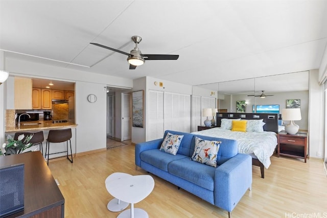 bedroom featuring baseboards, a sink, a ceiling fan, and light wood-style floors