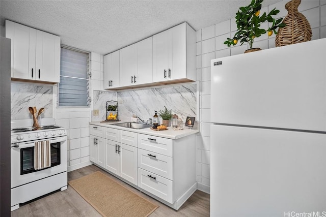 kitchen with light wood finished floors, light countertops, a sink, a textured ceiling, and white appliances