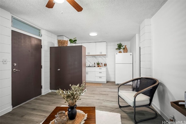 interior space featuring light wood-style flooring, white cabinetry, a textured ceiling, and freestanding refrigerator