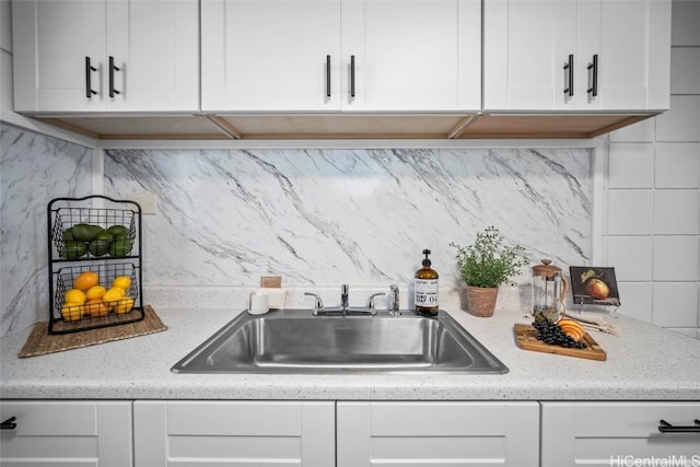 kitchen featuring tasteful backsplash, a sink, white cabinetry, and light stone countertops