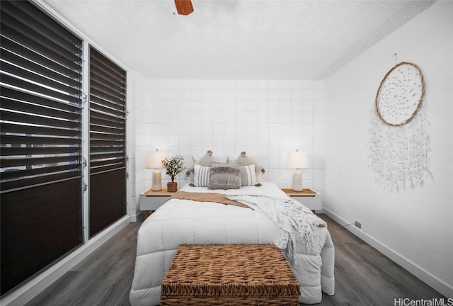 bedroom with dark wood-style floors, a textured ceiling, tile walls, and baseboards