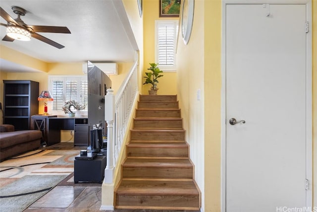 stairway featuring an AC wall unit and a ceiling fan