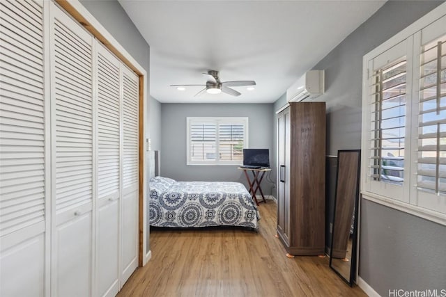 bedroom featuring a ceiling fan, wood finished floors, baseboards, and a wall mounted air conditioner