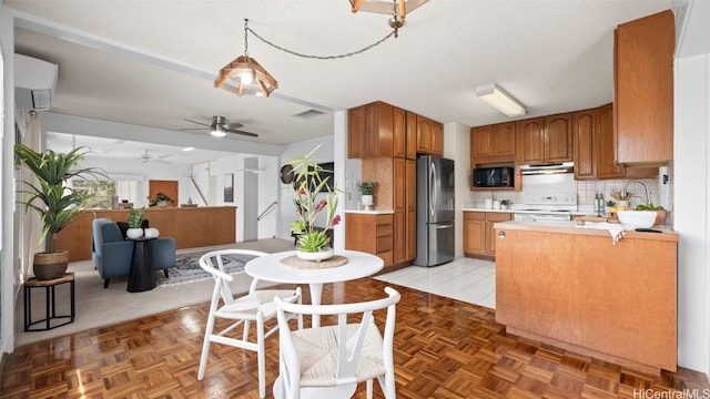 kitchen featuring black microwave, white range with electric cooktop, light countertops, freestanding refrigerator, and brown cabinetry