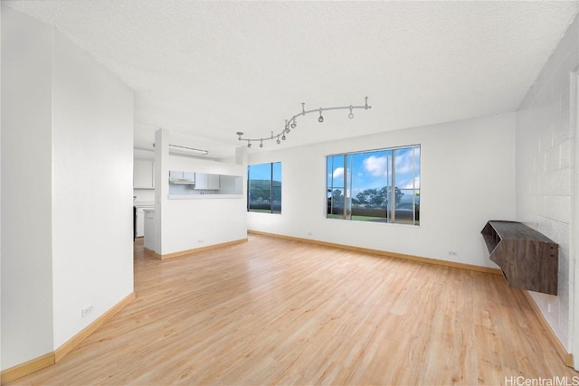 unfurnished living room with light wood finished floors, track lighting, a textured ceiling, and baseboards