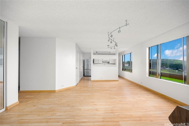 unfurnished living room featuring light wood finished floors, a textured ceiling, and baseboards