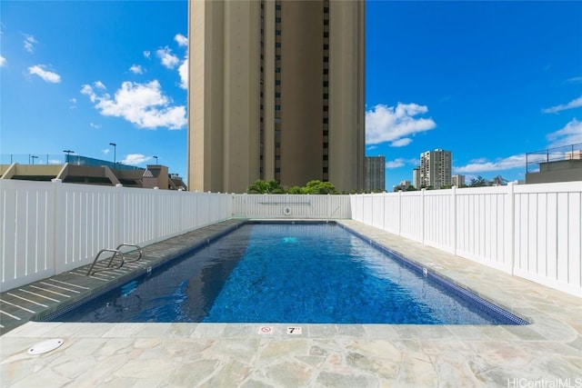 community pool with a patio, a fenced backyard, and a city view