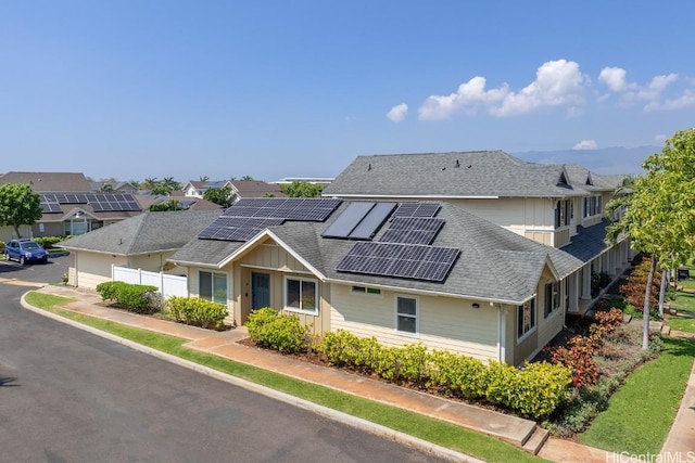 view of front of property with solar panels, a shingled roof, and fence