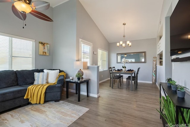 living area with high vaulted ceiling, baseboards, wood finished floors, and ceiling fan with notable chandelier