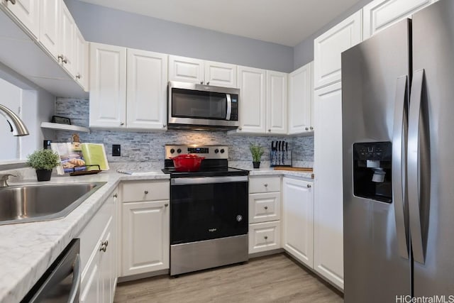 kitchen with stainless steel appliances, white cabinets, a sink, and tasteful backsplash