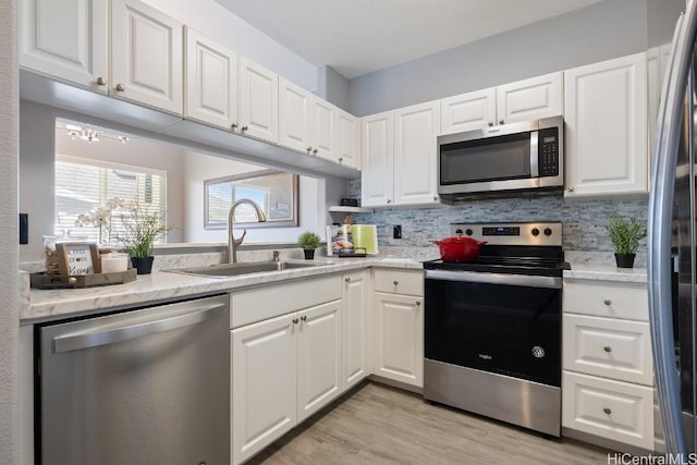 kitchen with light wood finished floors, stainless steel appliances, tasteful backsplash, white cabinets, and a sink