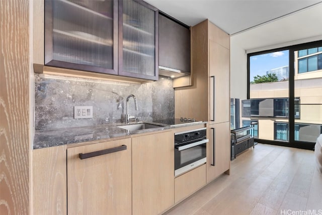 kitchen with wall oven, light brown cabinets, decorative backsplash, black electric cooktop, and a sink