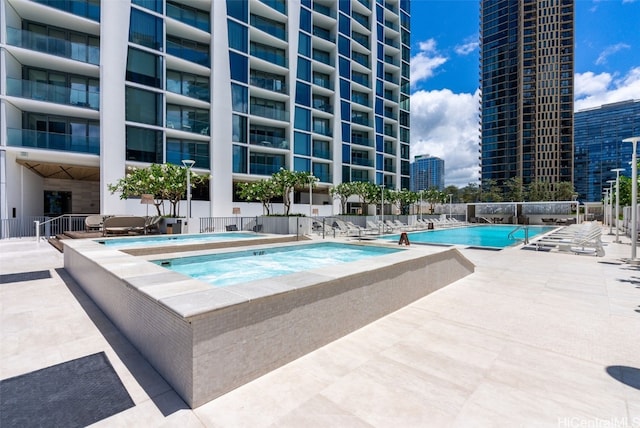 pool featuring a patio, a view of city, a community hot tub, and fence