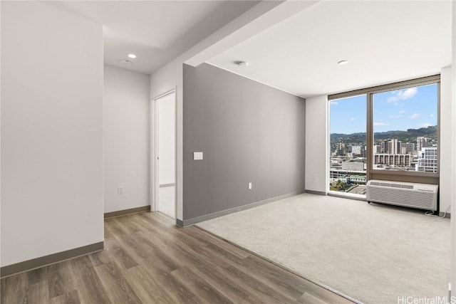 spare room featuring a view of city, baseboards, a wall of windows, and wood finished floors