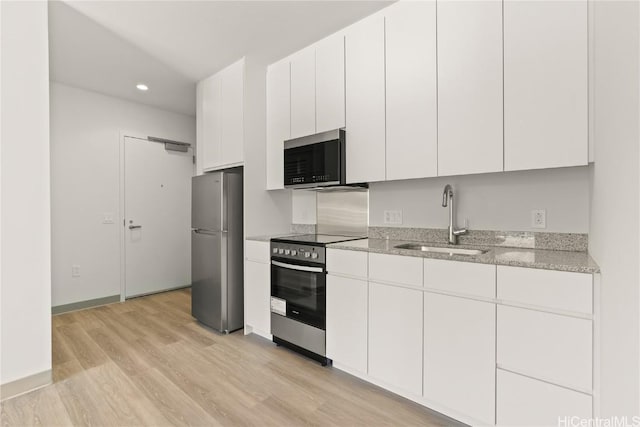 kitchen with light stone countertops, stainless steel appliances, light wood-type flooring, white cabinetry, and a sink