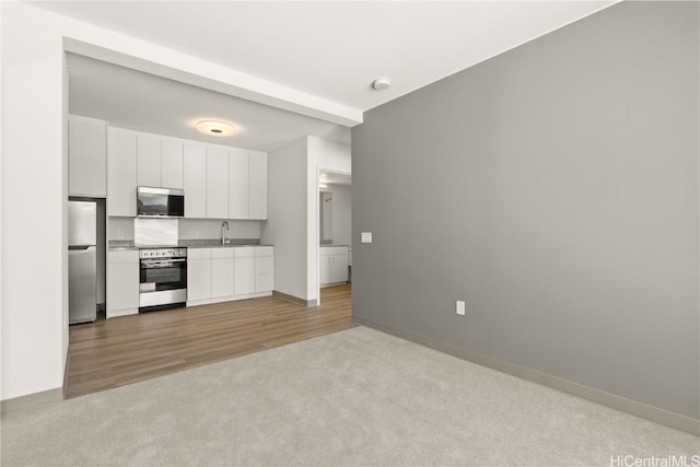 kitchen featuring baseboards, white cabinets, light colored carpet, stainless steel appliances, and a sink