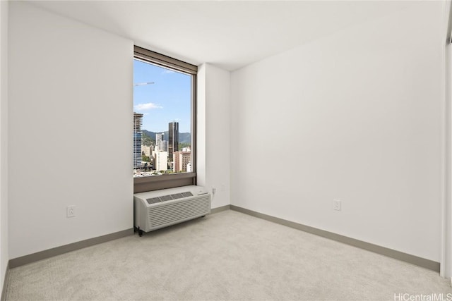 empty room featuring a city view, a wall mounted air conditioner, light carpet, and baseboards