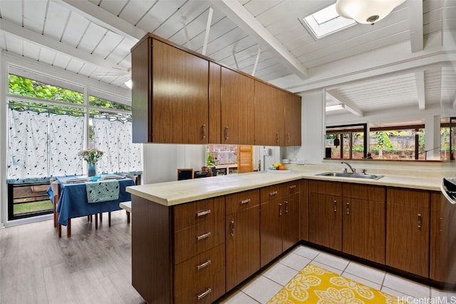 kitchen featuring a peninsula, a skylight, a sink, light countertops, and beam ceiling